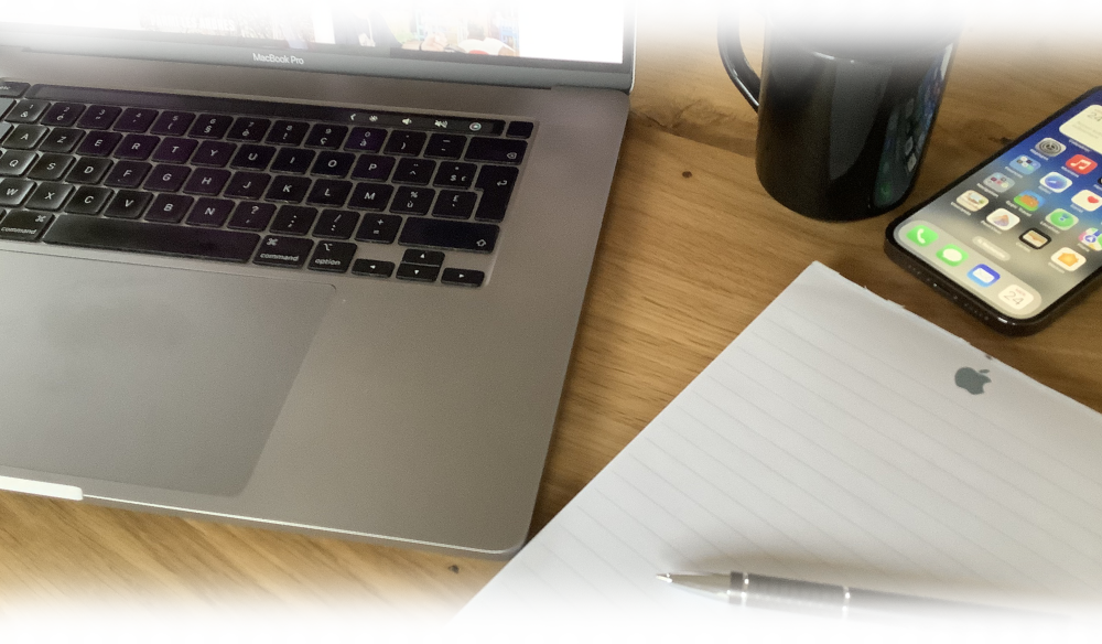 Mac et iPhone posÃ©s sur un bureau avec tasse de cafÃ©, carnet de prise de note et stylo juste Ã  cotÃ©